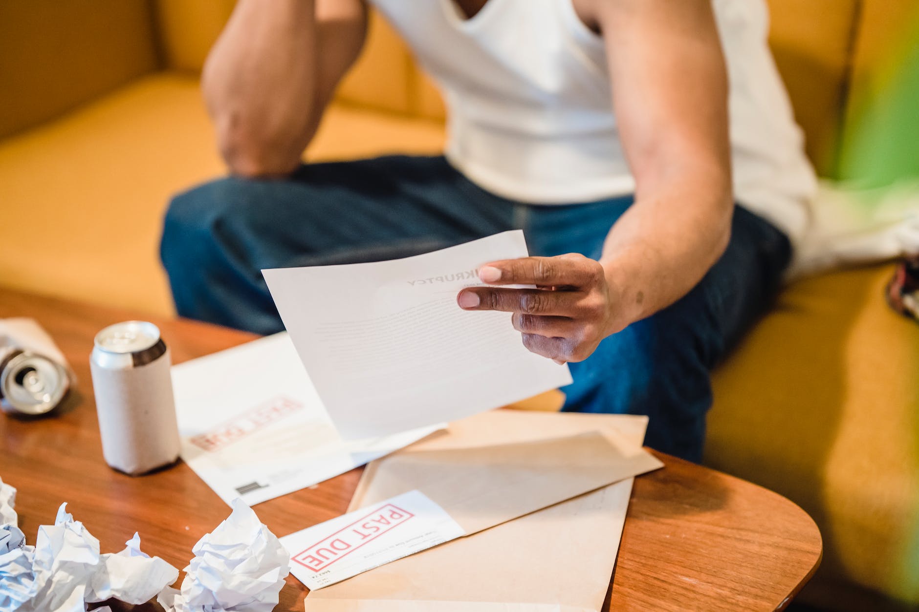 man sitting on sofa and reading unpaid bills